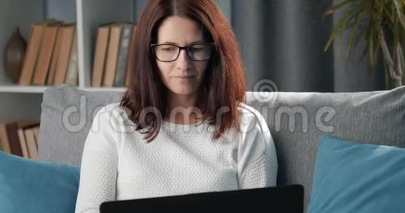 坐在沙发上用笔记本电脑工作的女人的肖像视频的预览图
