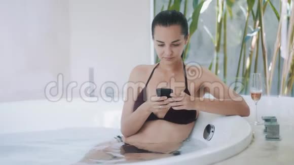 年轻女性使用智能手机坐在豪华公寓的现代圆形浴缸里视频的预览图