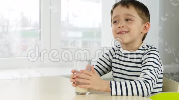 一个快乐的孩子坐在靠窗的桌子旁喝着杯子里的牛奶孩子体验情绪笑声视频的预览图