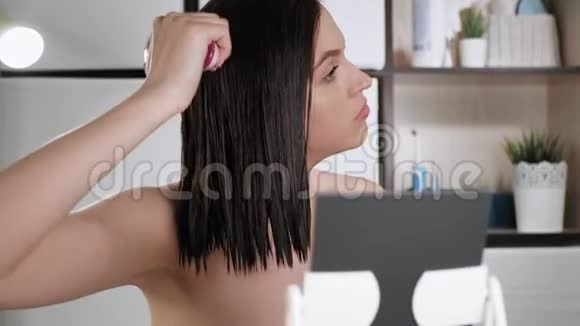女孩梳湿头发年轻女子正在浴室里裹毛巾用梳子梳着湿漉漉的头在家化妆头发视频的预览图