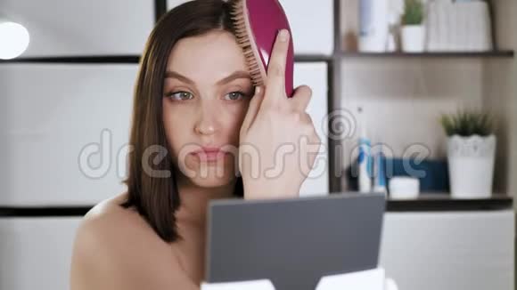女孩梳头浴室里有魅力的年轻女人照镜子用梳子梳她的干头发化妆视频的预览图