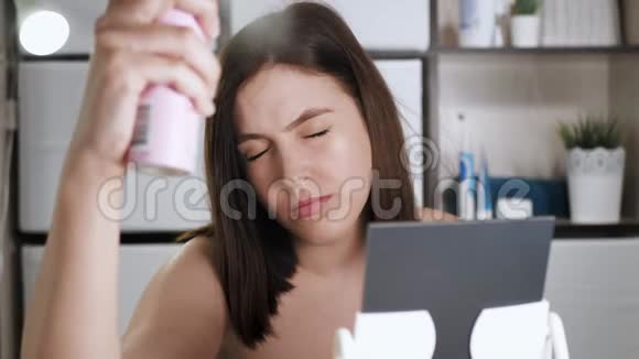 女孩用头发喷雾有魅力的女人在浴室里拿着带有清漆的喷雾瓶把它喷在头上视频的预览图