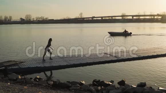 一个运动女孩跑在码头沿湖背景美丽的日落户外有氧运动运动动机视频的预览图