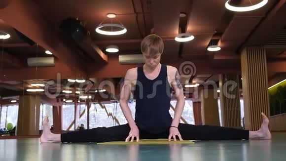 这个人在瑜伽课上做了垫子上的劈裂运动广角对称框架一个年轻英俊的男人视频的预览图