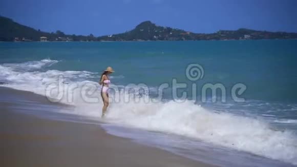 美丽的女孩戴着草帽背景是苏梅岛海滩上的大海浪视频的预览图