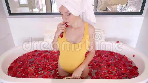 美丽的年轻女性在豪华的浴缸中充满玫瑰花瓣在浴缸中休闲视频的预览图