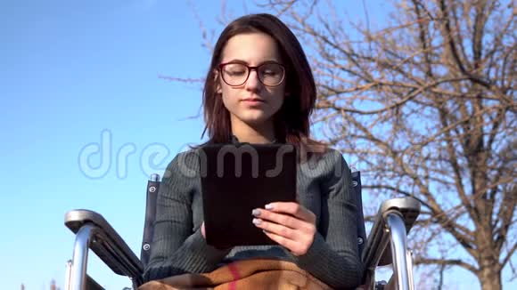 坐轮椅的年轻人拿着平板电脑自然界中的残疾人在平板电脑上通信视频的预览图