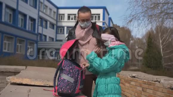 女儿和母亲戴着防护面具站在学校大楼外面女儿用防腐剂治疗双手视频的预览图