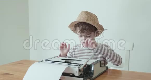 戴帽子的小男孩正在学习用一台旧的便携式打字机打字视频的预览图