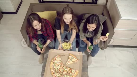年轻的女性朋友在家里看电影或电视上的体育比赛时喝啤酒吃披萨和零食视频的预览图