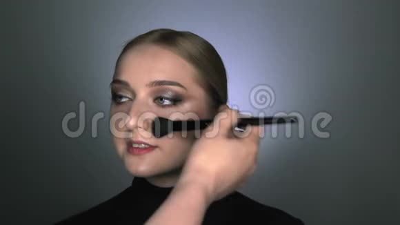 化妆师为美容工作室的年轻女性制作专业化妆化妆师用大大的腮红视频的预览图