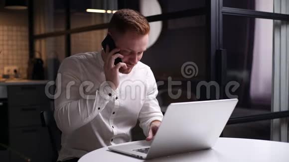 忙碌的英俊的年轻人坐在桌子旁手提电脑打电话视频的预览图