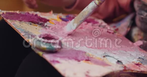 关闭艺术家调色板与粉红色黄色白色和紫色的颜色在上面艺术调色板的混合点和视频的预览图