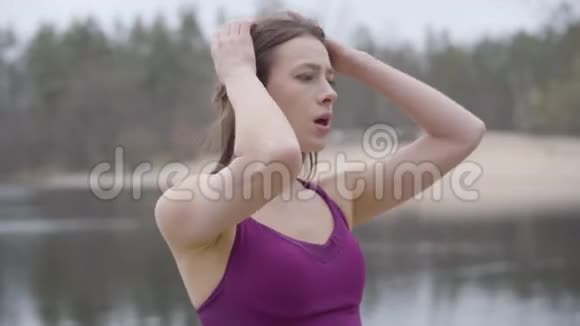 精疲力竭的白人女孩在湖岸上呼吸沉重疲惫的女跑步者在锻炼中休息的肖像视频的预览图