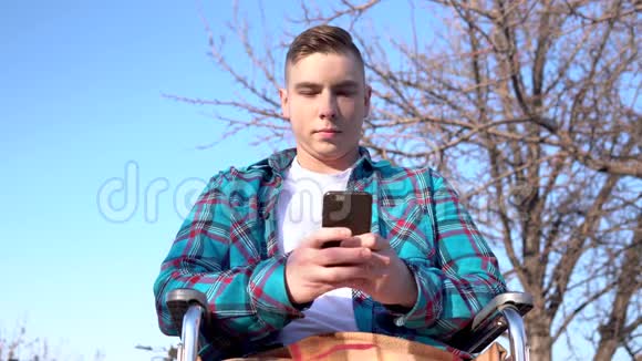 坐轮椅的年轻人拿着电话自然界中的残疾人在智能手机上通信视频的预览图