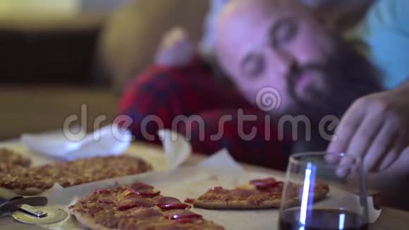 几个男人和女人晚上在客厅的沙发上吃披萨同时在电视上看电影概念视频的预览图