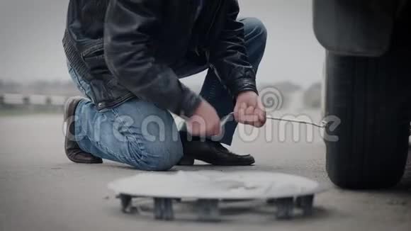 一个拿着千斤顶的人把车放下在一条荒芜的道路上更换车轮视频的预览图
