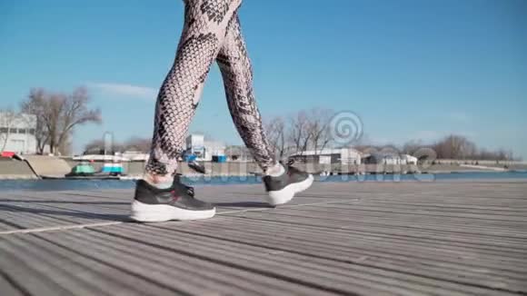 快关门穿着运动服和黑色运动鞋的年轻苗条女孩在湖边的码头上慢动作视频的预览图