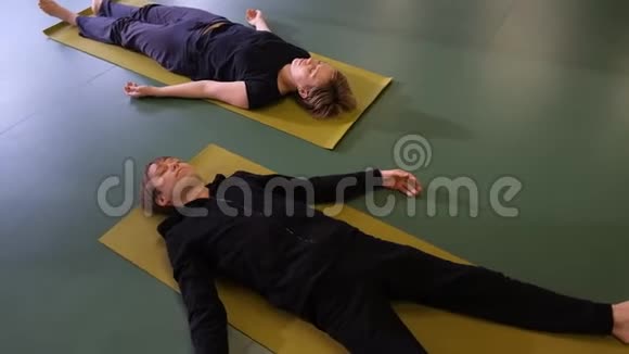 瑜伽中的沙瓦萨纳一个年轻的男人和女人闭着眼睛躺在垫子上他们是放松和解放的视频的预览图