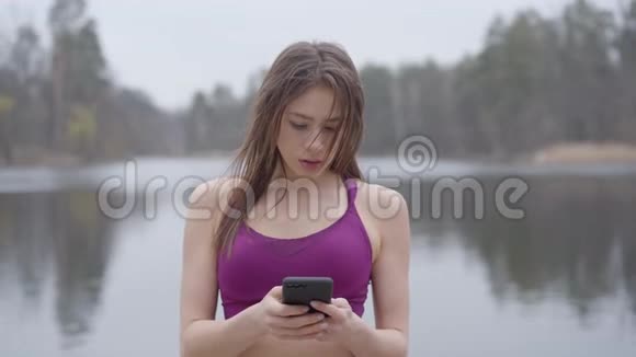 迷人的年轻白种人女士穿着紫色运动服使用智能手机和微笑的肖像阳性的深色头发视频的预览图