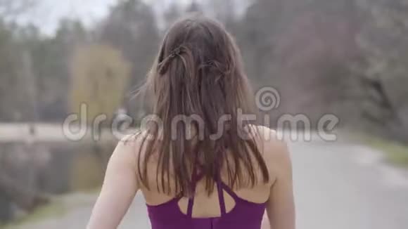 年轻健康的高加索女人在湖岸公园慢跑从小巷里走过的黝黑苗条女孩的后景视频的预览图