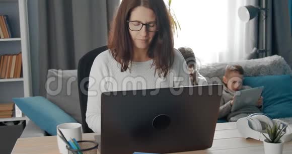 戴眼镜的自信女士带着孩子在笔记本电脑上工作视频的预览图
