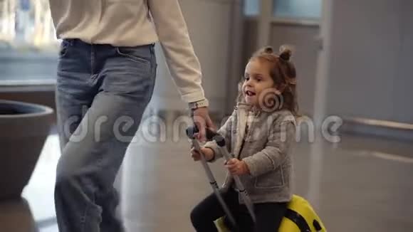 机场候机楼年轻的无法辨认的母亲骑着她可爱的女儿在一个小黄色的手提箱妈妈是黄色的视频的预览图
