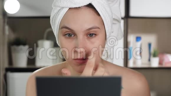 眼霜年轻漂亮的女人在她的左眼下面涂上奶油女孩在浴室里照镜子视频的预览图