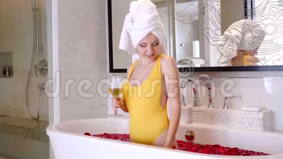 年轻貌美的女人在浴缸里拿着香槟和玫瑰花瓣视频的预览图