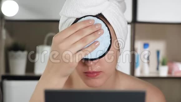 女孩用海绵擦她的脸浴室里漂亮的女人头上戴着毛巾照镜子洗脸视频的预览图