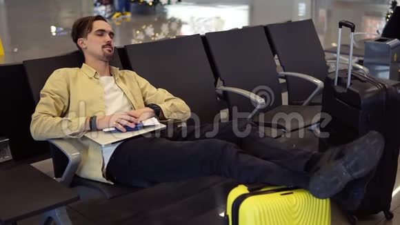 一个长胡子的人穿着黄色衬衫双腿躺在黄色的手提箱上在机场休息室里拿着他的东西视频的预览图