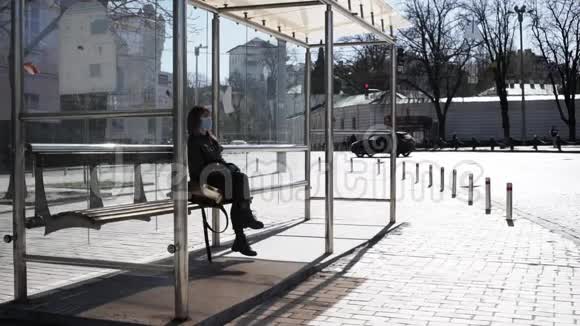 戴着外科口罩和乳胶手套的白人女性独自坐在公共汽车站视频的预览图