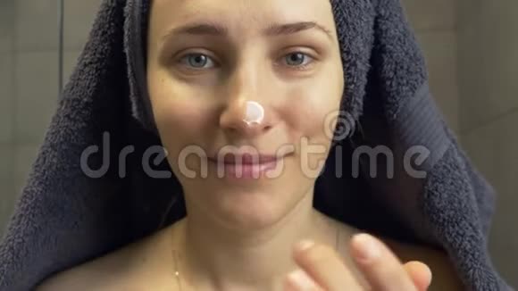 头上有毛巾的女人在脸上涂上护肤霜淋浴后照镜子女性保湿提升视频的预览图