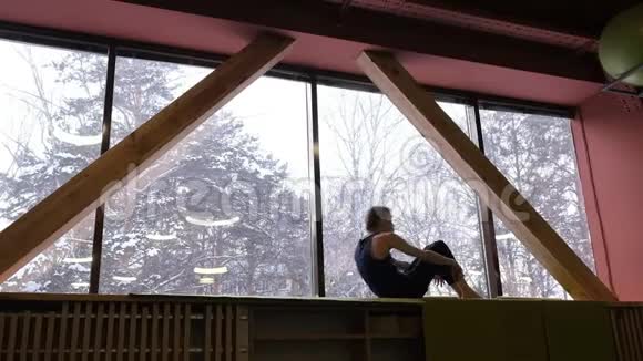 一个年轻的白人正在一扇大窗户附近做普拉提他躺在背上双腿弯在头后外部视频的预览图