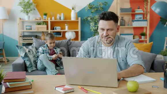 爸爸坐在办公桌前用电脑儿子走近他在家说话视频的预览图