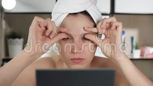 面部皮肤按摩带毛巾和镜子的漂亮女孩用手在眼睛上做面部按摩视频的预览图
