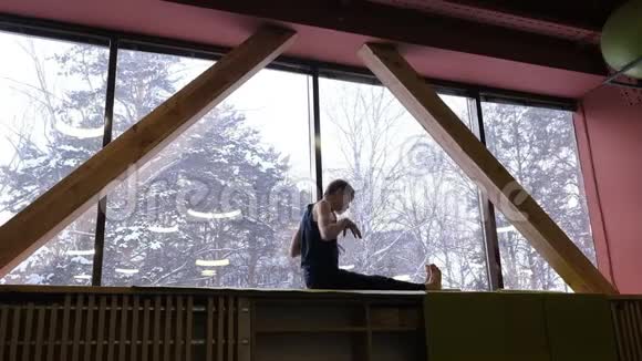 一个好男人在大窗户的窗台上做瑜伽窗外是冬林和日光广角视频的预览图