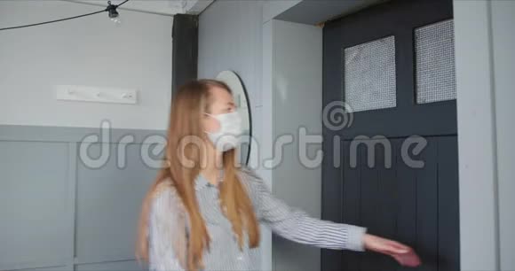年轻的金发女子戴着外科口罩打开门在自我隔离锁定期间从快递员那里接收投递箱视频的预览图