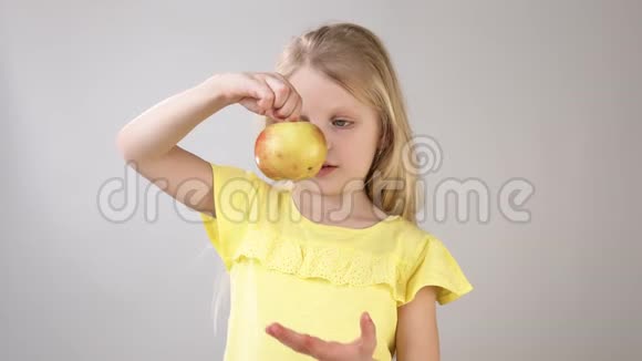 带苹果的女孩小女孩在白色背景上穿着黄色明亮的裙子吃苹果女孩视频的预览图