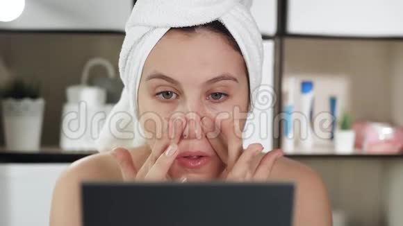 面部皮肤按摩有魅力的女孩在浴室用毛巾和镜子做面部按摩在鼻子的颧骨部位视频的预览图