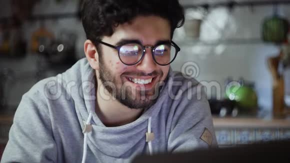 一个快乐的男人晚上在厨房里用笔记本电脑工作视频的预览图