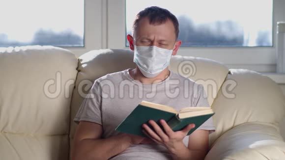 戴着医疗面具的男人手里拿着一本书坐在沙发上看着相机视频的预览图