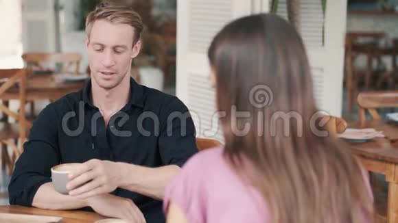 年轻夫妇在咖啡馆喝咖啡男人和女孩谈笑风生视频的预览图