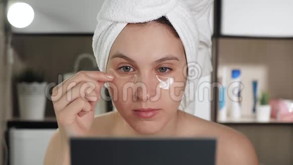 浴室里的女孩头上戴着毛巾看着镜子移除眼睛补丁卫生美容化妆面部护理视频的预览图
