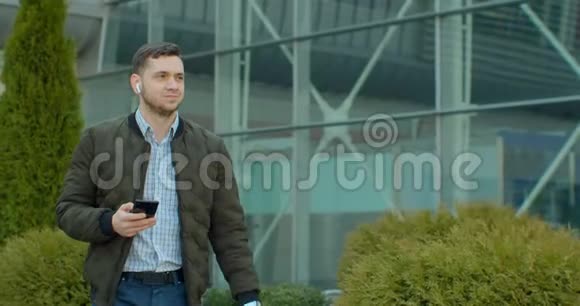 在现代办公中心附近用智能手机行走的人的肖像在社交网络里和他的朋友聊天看上去视频的预览图