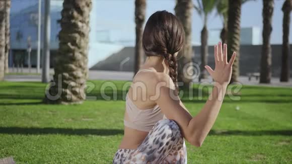 女人坐在垫子上做脊椎扭转姿势在公园里做瑜伽的女孩视频的预览图