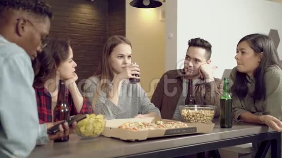 快乐的多民族朋友在家客厅喝啤酒吃披萨交流视频的预览图