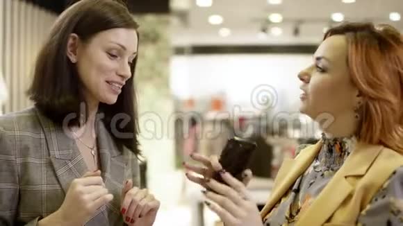 两个年轻的女性朋友正在服装店消磨时间其中一个正在把照片放在她的智能手机上视频的预览图