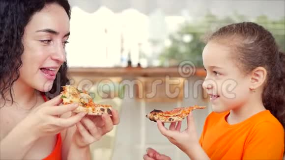 快乐的微笑轻松的年轻一家人急切地吃着美味的披萨女儿和母亲坐在桌子旁急切地吃着视频的预览图