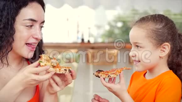 美丽的小女孩卷发和妈妈坐在餐桌旁吃意大利披萨看着每一个人视频的预览图